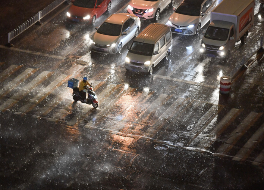 2021年4月15日傍晚，在天津市南开区，外卖骑手在风雨中骑行过马路。

