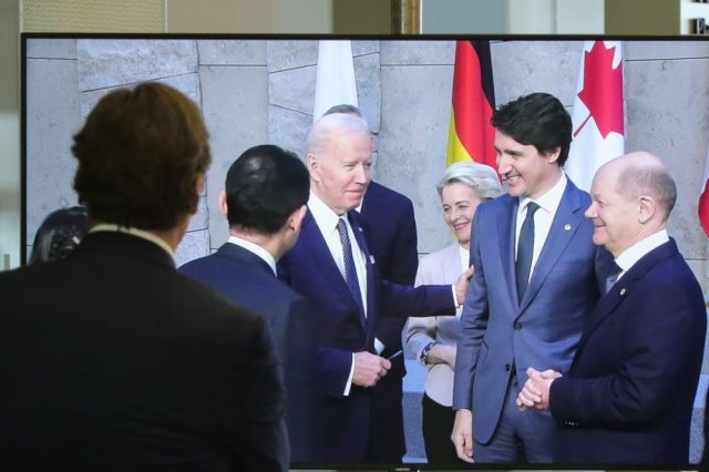 3月24日，在比利时布鲁塞尔的北约总部，一名男子观看屏幕上美国总统拜登（右四）、欧盟委员会主席冯德莱恩（右三）、加拿大总理特鲁多（右二）、德国总理朔尔茨（右一）出席七国集团峰会合影仪式的画面。新华社记者郑焕松摄