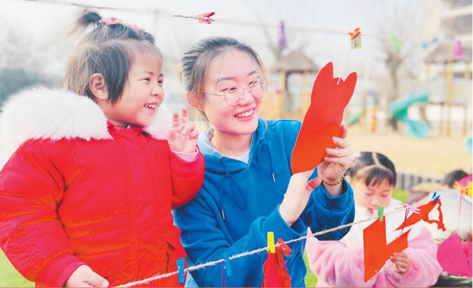 大村中心幼儿园的小朋友和老师一起看新学期祝福贺卡。