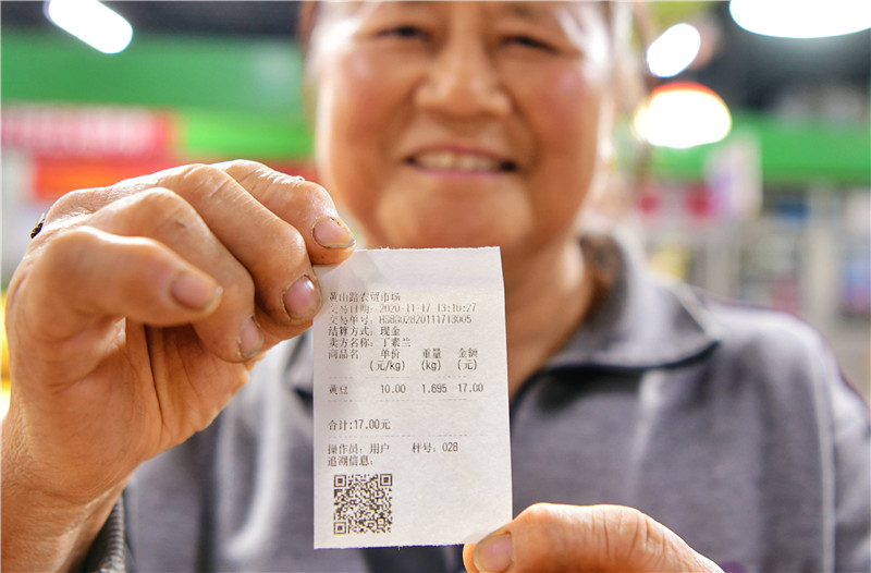 蔬菜商户向记者展示智能秤打印出的可追溯小票。