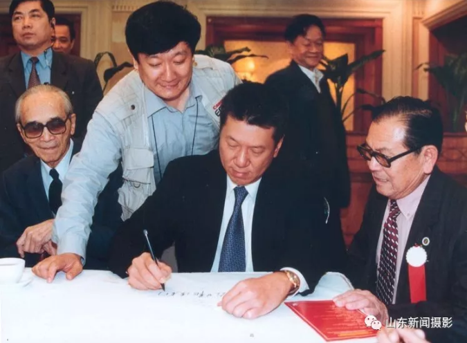 1999年12月16日晚6时，何厚铧为大众日报报题词。（前排左二为大众日报记者钱捍）