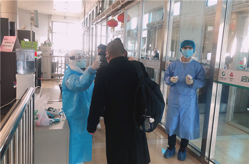2月2日上午10点，在淄博火车站进站口，穿着防护服、戴着护目镜的志愿者田娜娜，拿着体温枪为一名女士测体温。