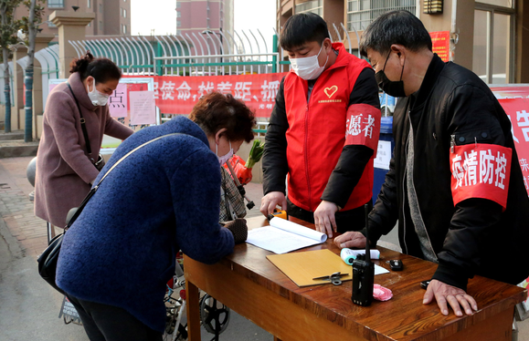 2月4日，在枣庄市市中区光明路街道陈庄社区大门口，党员志愿者、青年志愿者在对进入小区的人员进行信息登记、体温检测。
