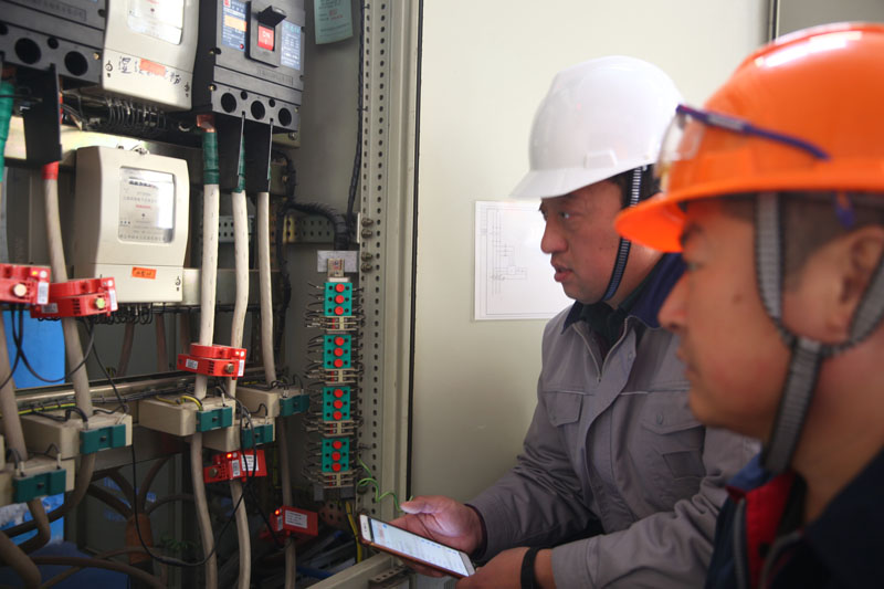 刘冰（左一）和企业负责人一起通过手机端用电监管系统查找故障。