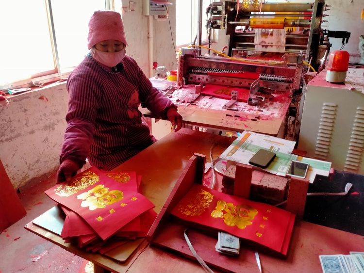 在生产线一端，工人将烫金后的双面红纸放到一边。