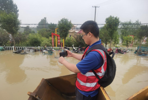 大众日报记者赵丰在河南尉氏县救援一线采访，站在铲车大铲斗上进行现场报道。