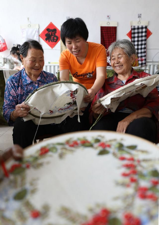 8月2日，沂南县大庄镇杨家坡村，冯树英（中）在她的刺绣工作室指导村里老人刺绣，她们制作的绣品将出口海外。