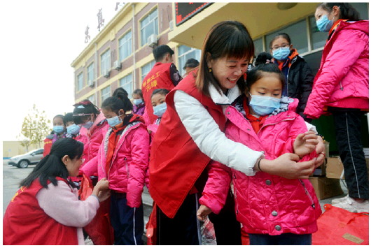 无棣县慈善义工协会的志愿者为该县西小王镇中心小学的学生穿上捐赠的羽绒服。
