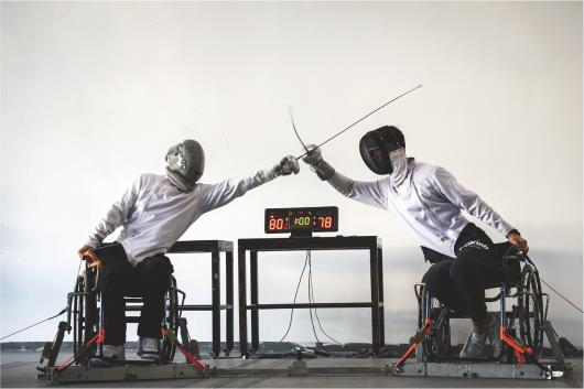 青岛市红岛奥体中心训练馆内，轮椅上的魏林（左）与教练实战练习，魏林成绩领先。